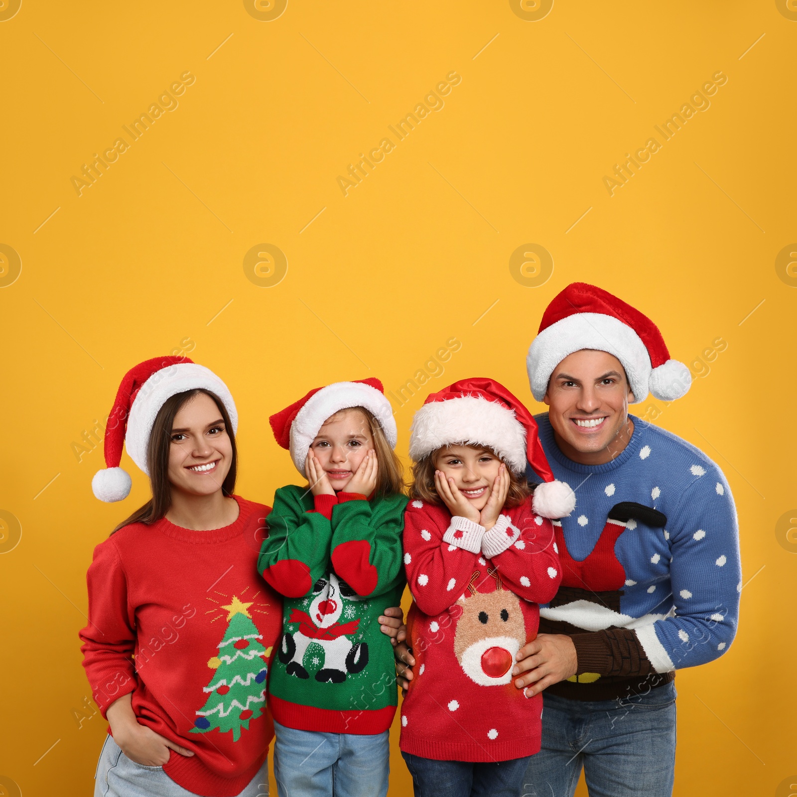Photo of Family in Christmas sweaters and Santa hats on yellow background