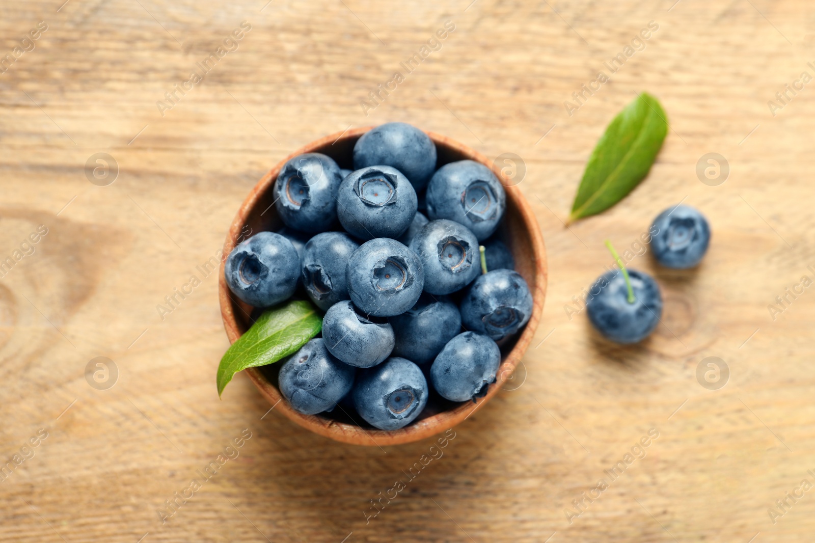 Photo of Bowl of fresh tasty blueberries on wooden table, flat lay