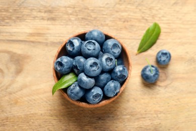 Bowl of fresh tasty blueberries on wooden table, flat lay
