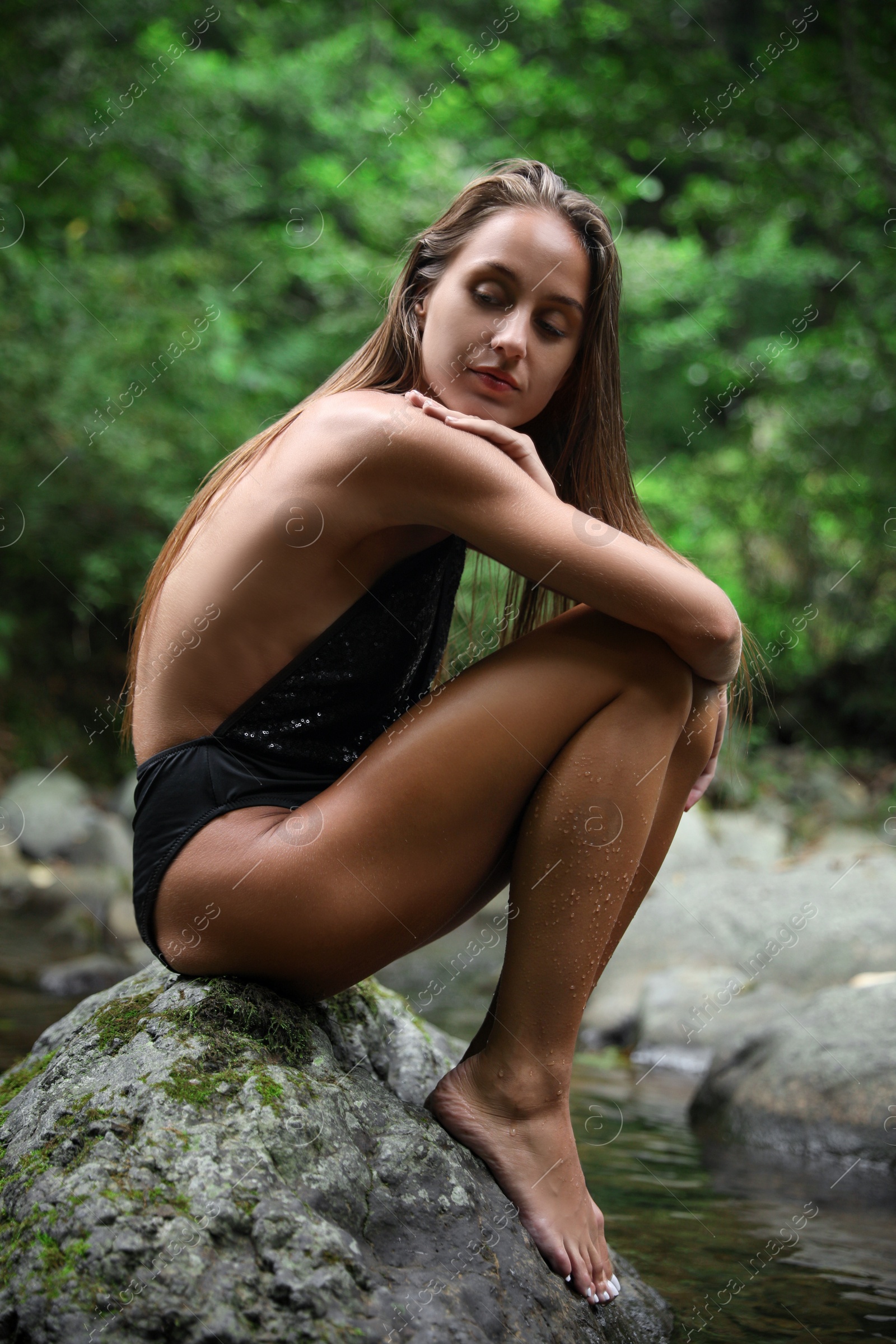 Photo of Beautiful young woman sitting on rock near mountain river outdoors