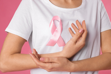 Woman with pink ribbon on color background, closeup. Breast cancer awareness