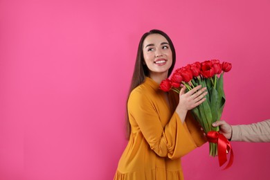 Photo of Happy woman receiving red tulip bouquet from man on pink background, space for text. 8th of March celebration