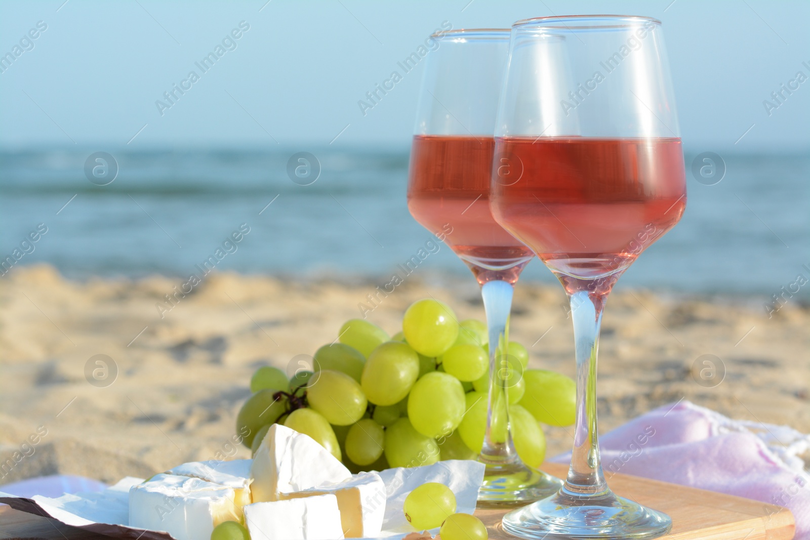 Photo of Glasses with rose wine and snacks on sandy seashore, closeup. Space for text