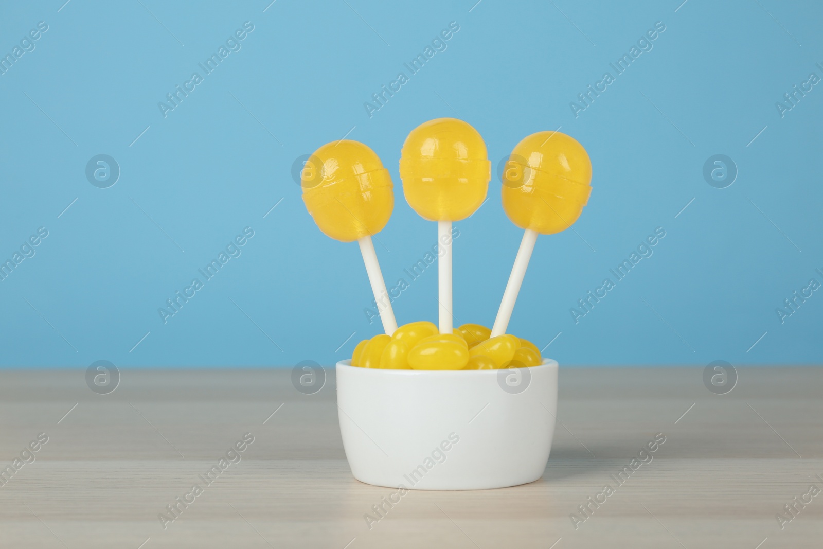 Photo of Delicious lemon drops and lollipops on wooden table against light blue background