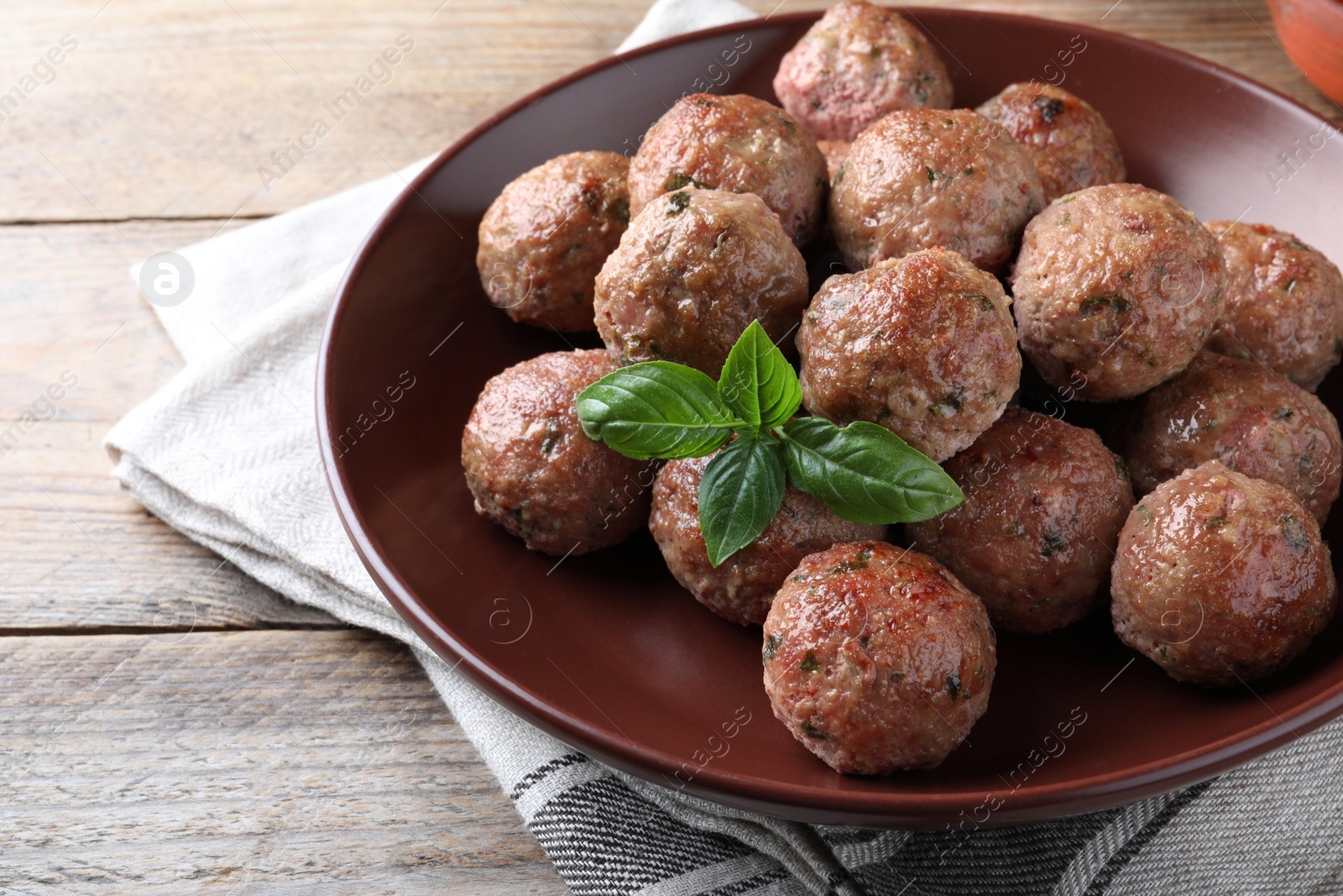 Photo of Tasty cooked meatballs with basil served on wooden table