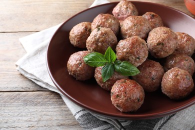 Photo of Tasty cooked meatballs with basil served on wooden table