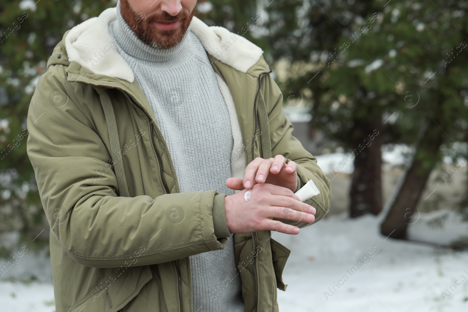 Photo of Man applying cream from tube onto hand outdoors, closeup. Winter care