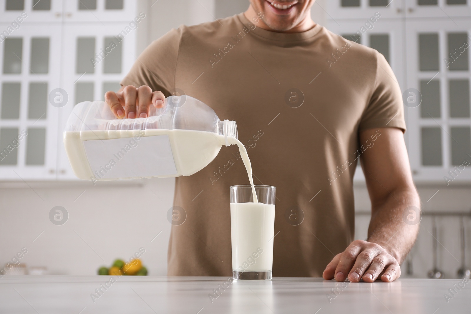 Photo of Man pouring milk from gallon bottle into glass at white marble table in kitchen, closeup