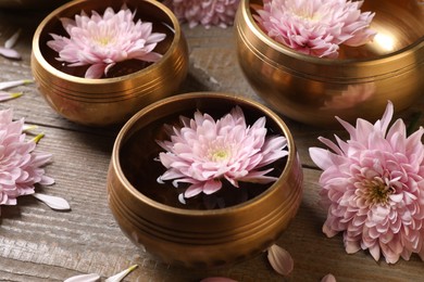 Photo of Tibetan singing bowls with water and beautiful flowers on wooden table, closeup