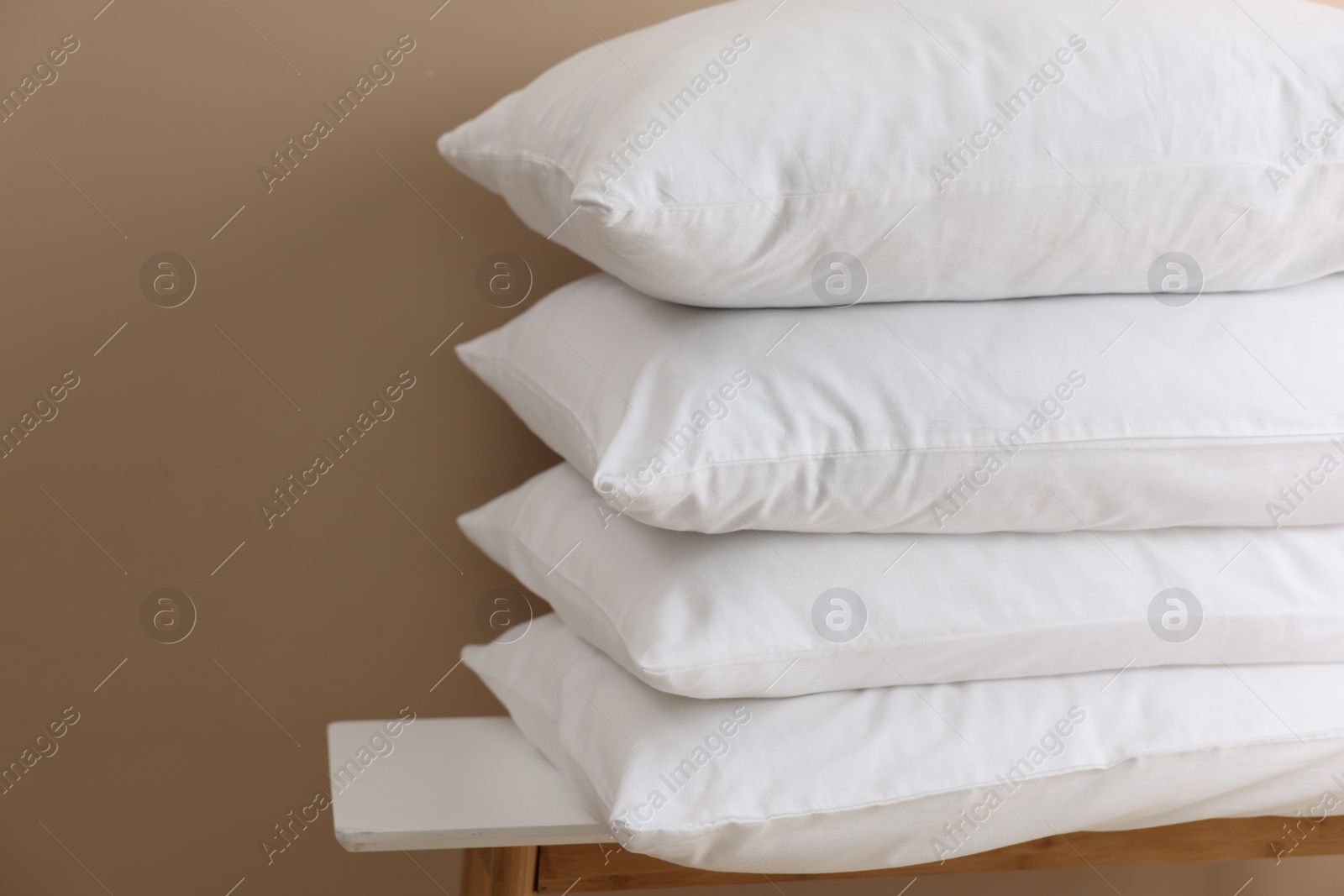 Photo of Stack of soft white pillows on table near beige wall. Space for text