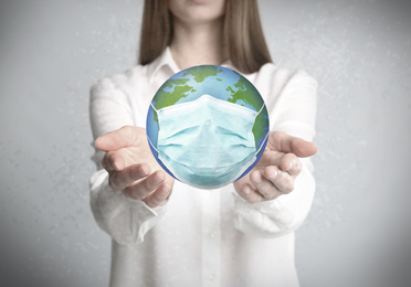 Woman holding Earth with medical mask on light background, closeup. Concept of coronavirus outbreak