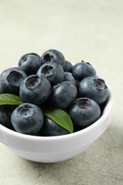 Photo of Bowl of fresh tasty blueberries on light grey table, closeup