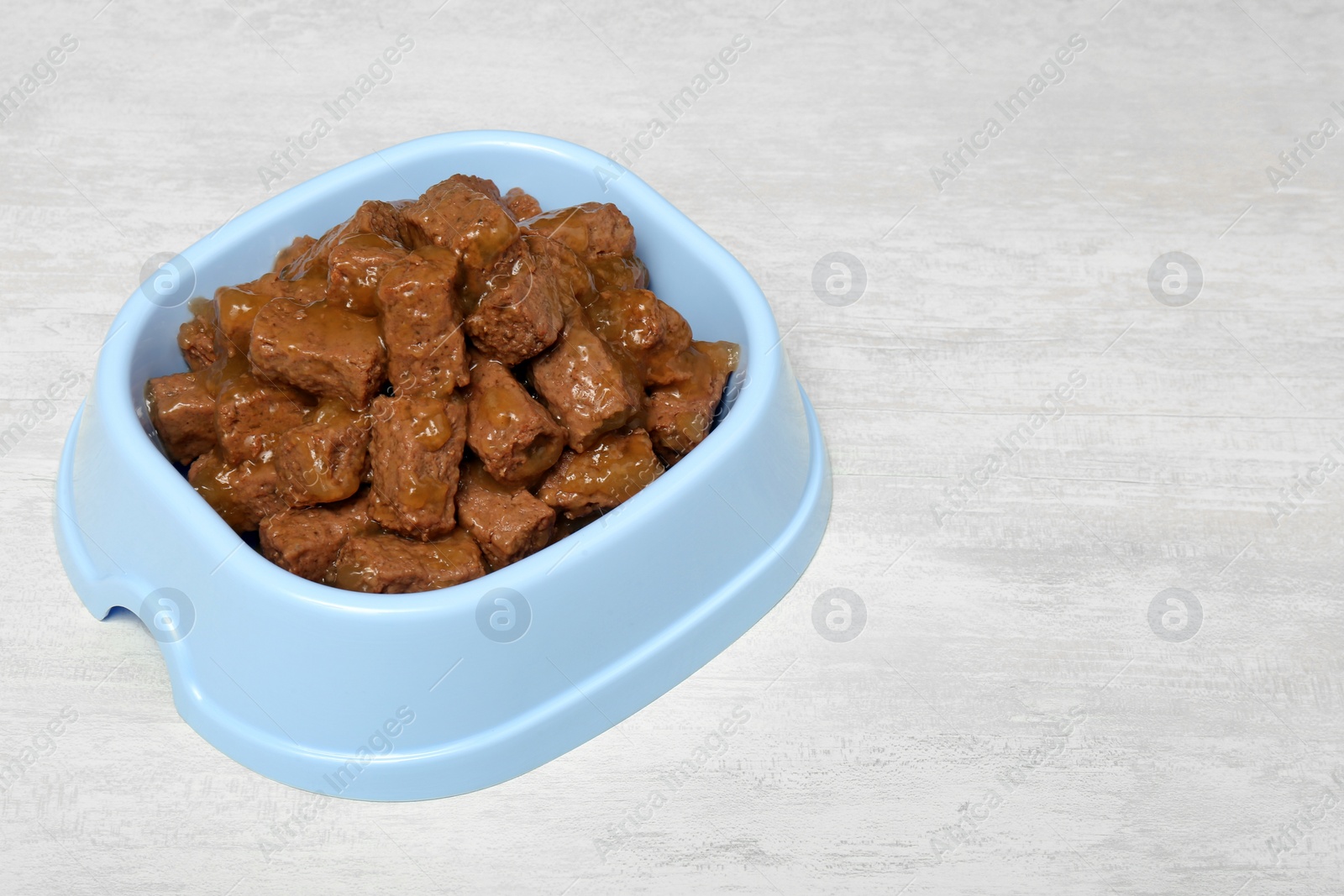 Photo of Wet pet food in feeding bowl on white table, space for text