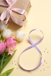 Photo of 8th of March greeting card design with violet ribbon, gift box and beautiful flowers on beige background. International Women's day