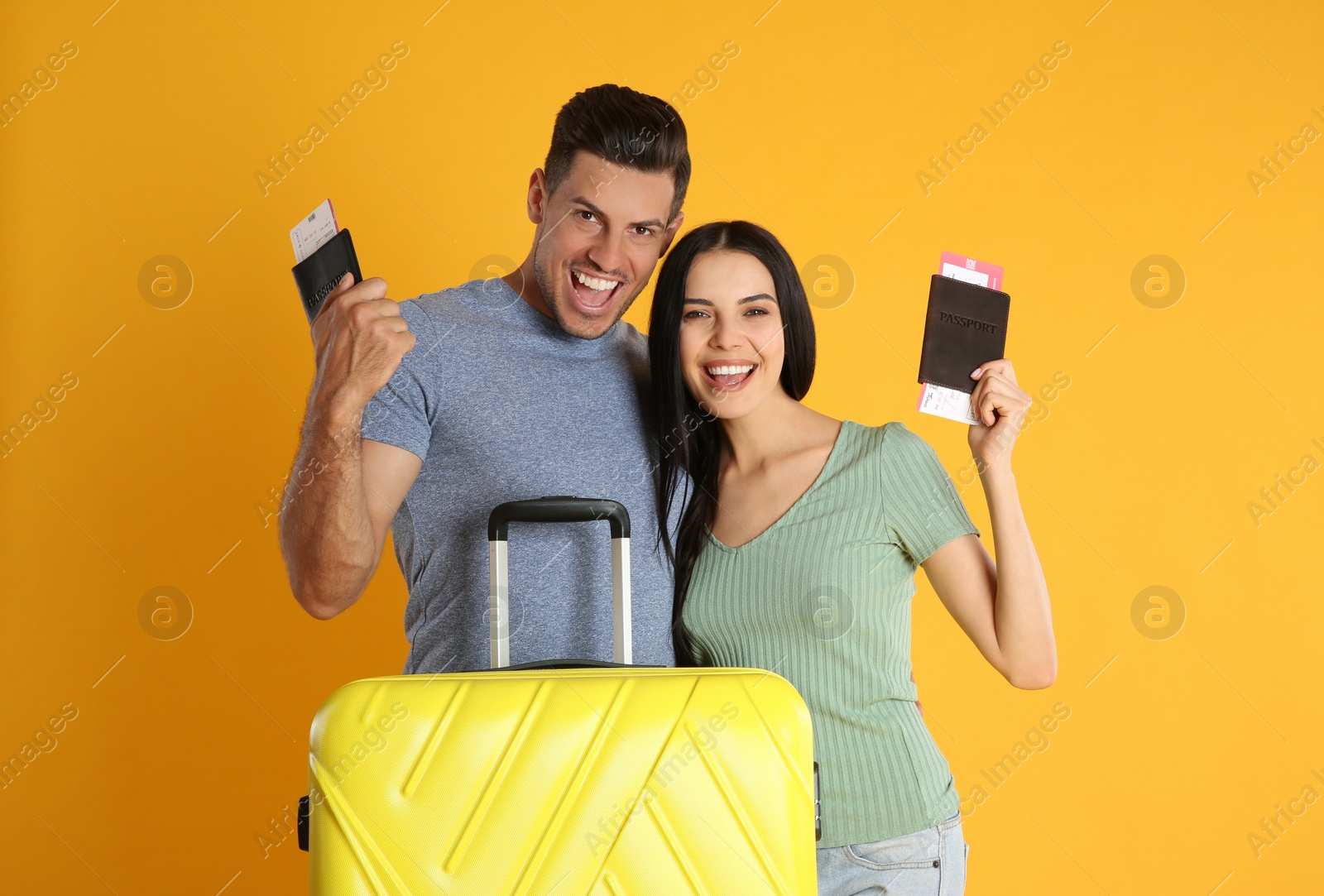 Photo of Happy couple with suitcase and tickets in passports for summer trip on yellow background. Vacation travel