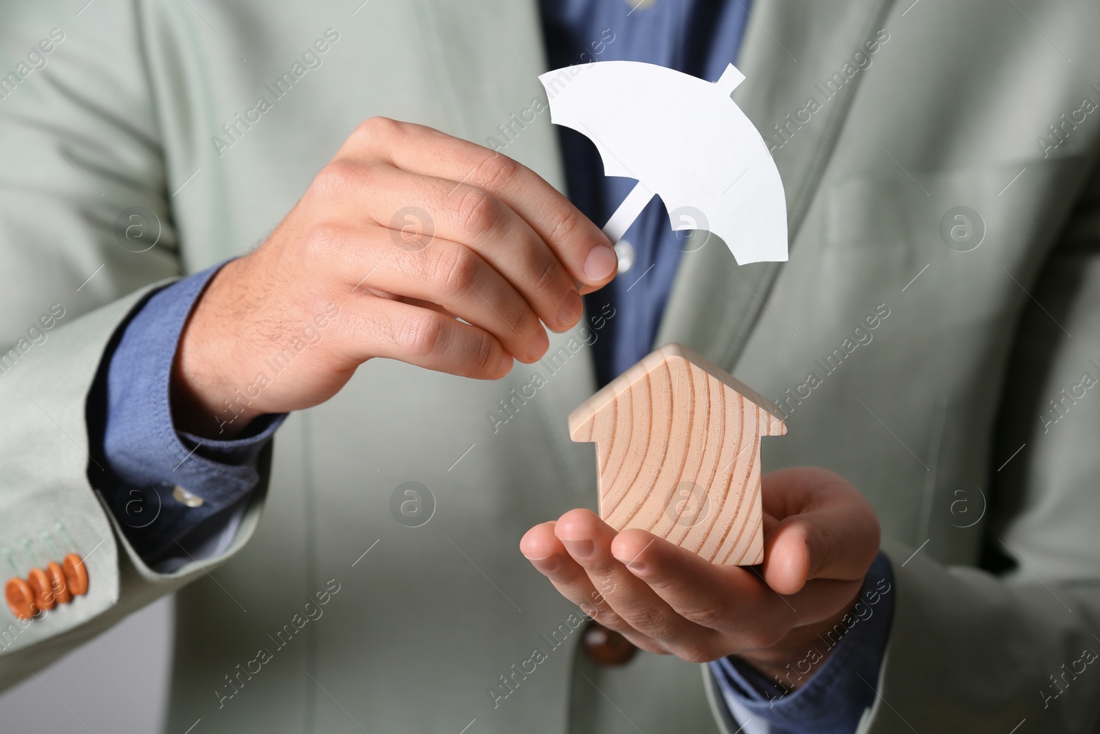 Photo of Male agent covering wooden house with umbrella cutout, closeup. Home insurance