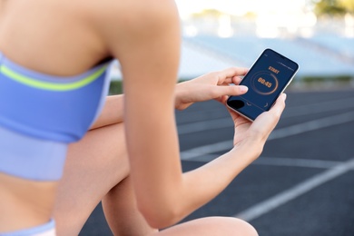Photo of Young woman using fitness app on smartphone at stadium, closeup