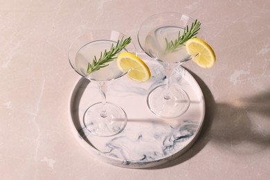 Photo of Tray with martini glasses of fresh cocktail, rosemary and lemon slices on beige marble table