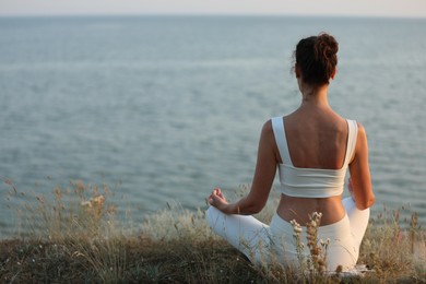 Woman meditating near sea, back view. Space for text