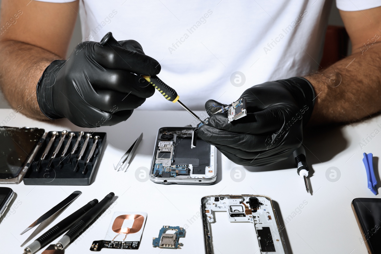 Photo of Technician repairing broken smartphone at white table, closeup