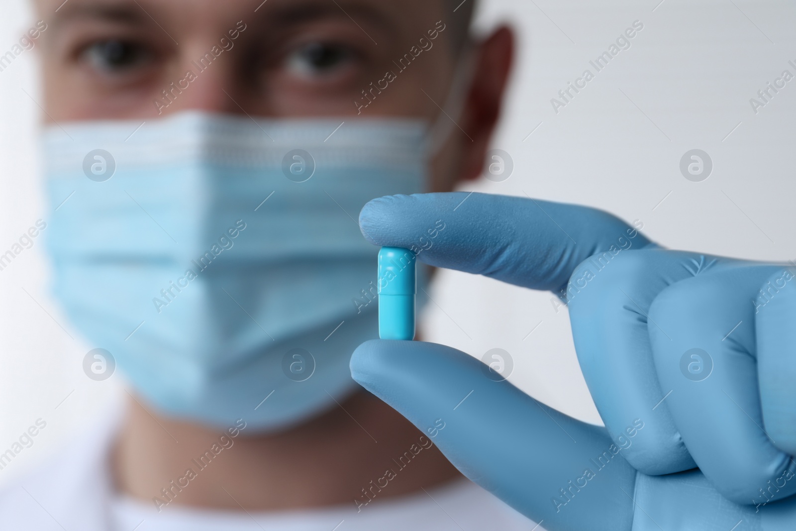 Photo of Doctor holding pill on light background, selective focus