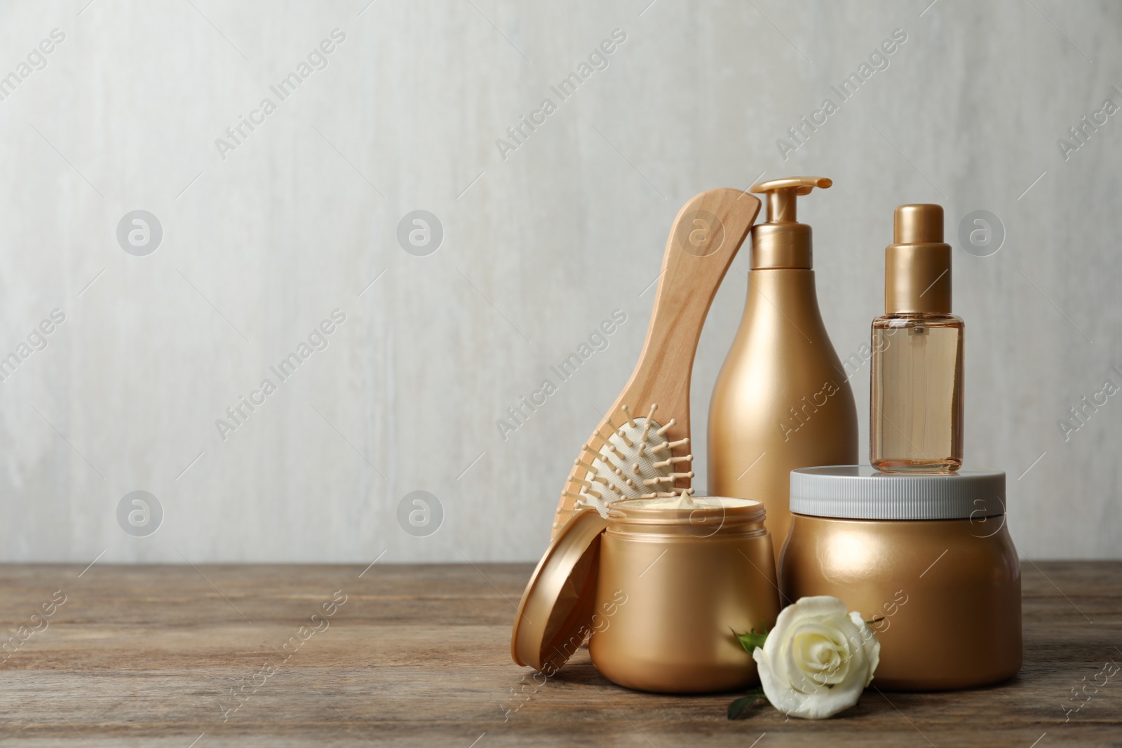 Photo of Different hair products, flower and brush on wooden table. Space for text