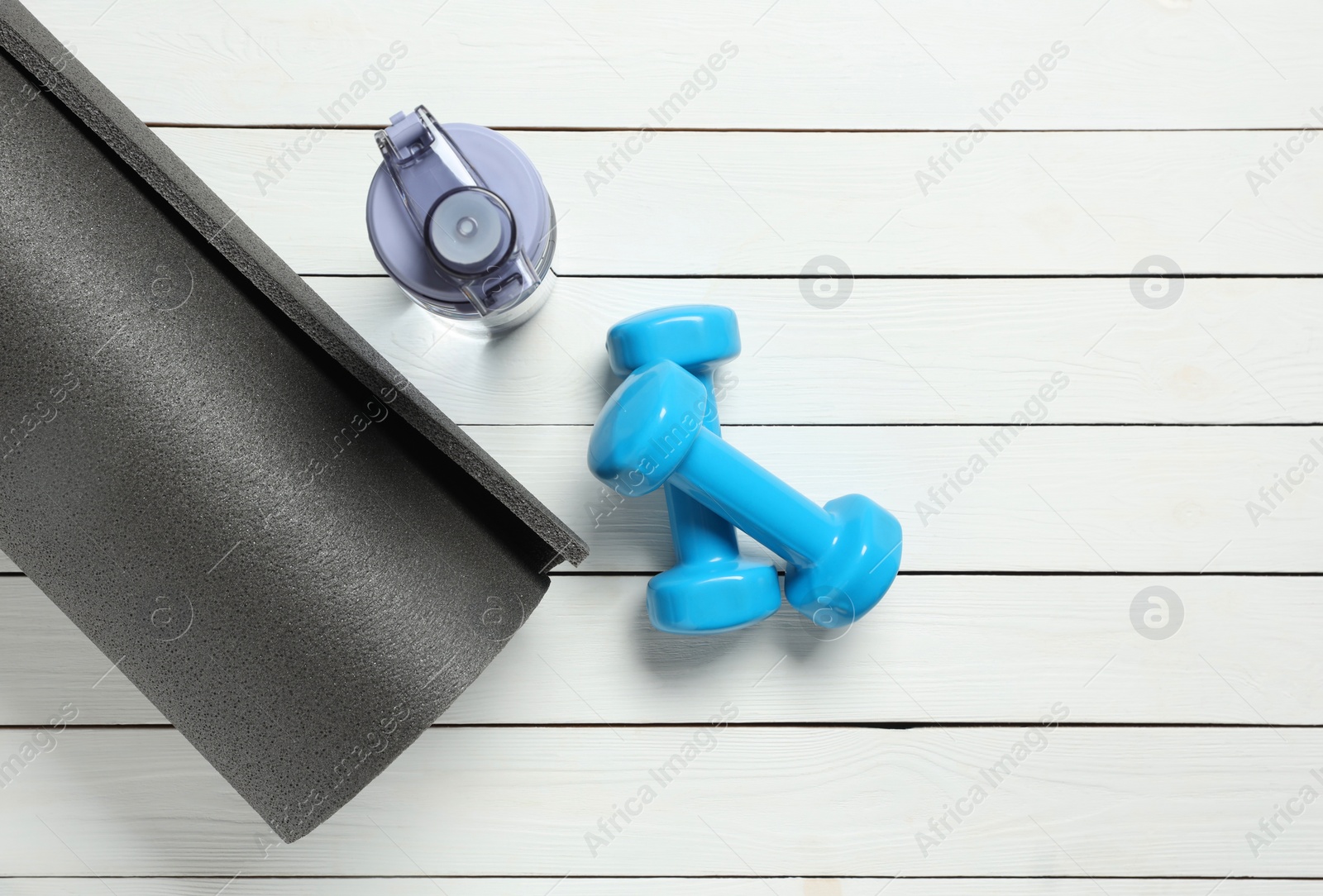 Photo of Yoga mat, dumbbells and bottle of water on white wooden floor, flat lay. Space for text