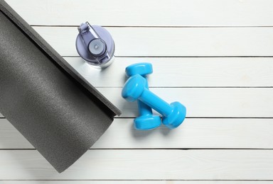 Yoga mat, dumbbells and bottle of water on white wooden floor, flat lay. Space for text