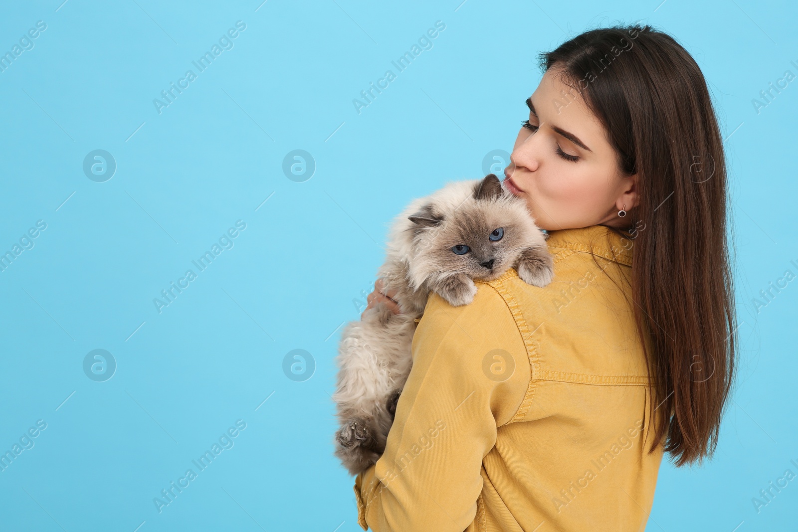 Photo of Woman kissing her cute cat on light blue background, space for text