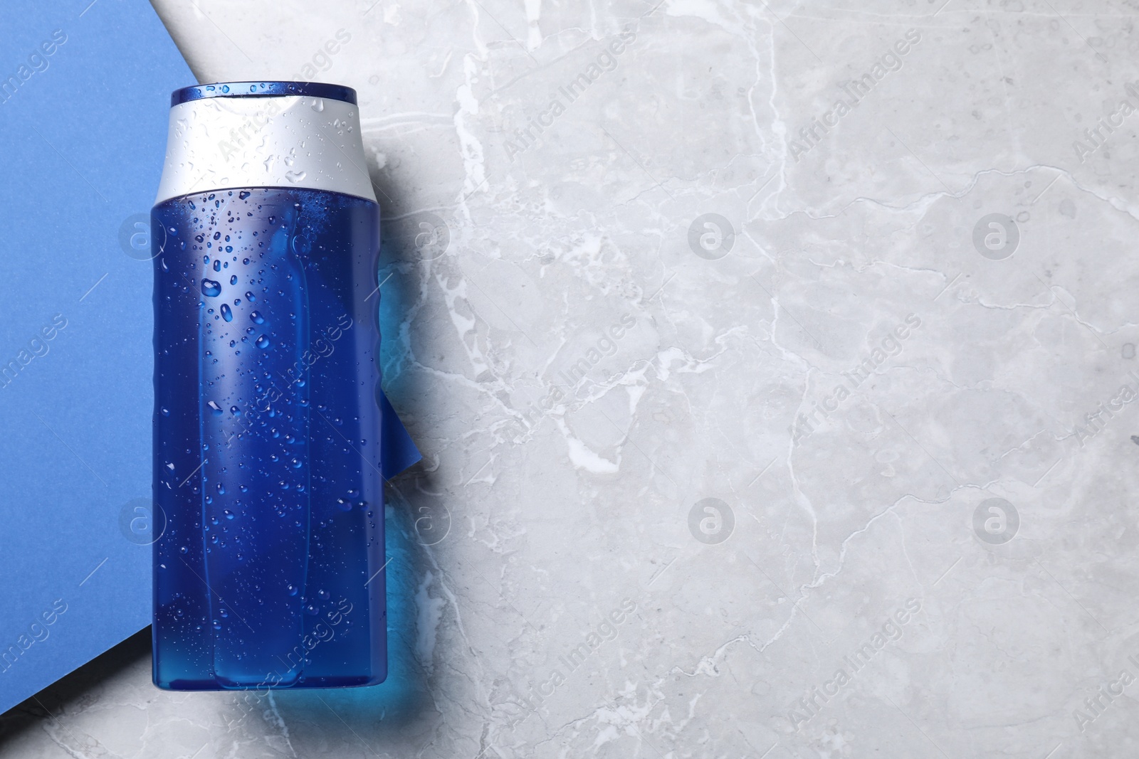 Photo of Top view of blue bottle with water drops on color background, space for text. Men's cosmetics