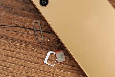 Photo of SIM card, mobile phone and ejector on wooden table, flat lay