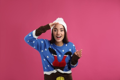 Photo of Surprised young woman in Christmas sweater and hat on pink background