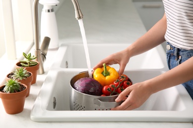 Photo of Woman washing fresh vegetables in kitchen sink, closeup