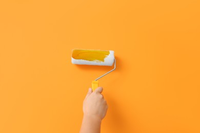 Photo of Worker using roller to paint wall with orange dye, closeup