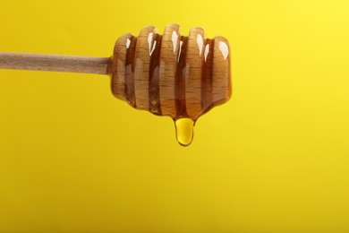 Photo of Delicious honey flowing down from dipper against yellow background, closeup. Space for text