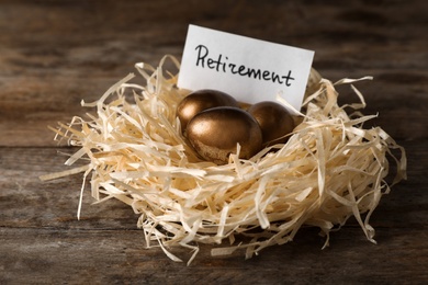 Photo of Golden eggs and card with word RETIREMENT in nest on wooden background. Pension concept