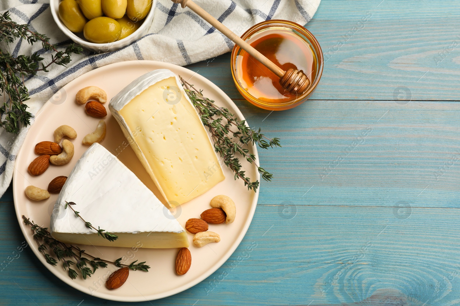 Photo of Tasty Camembert cheese with thyme, honey and nuts on light blue wooden table, flat lay. Space for text