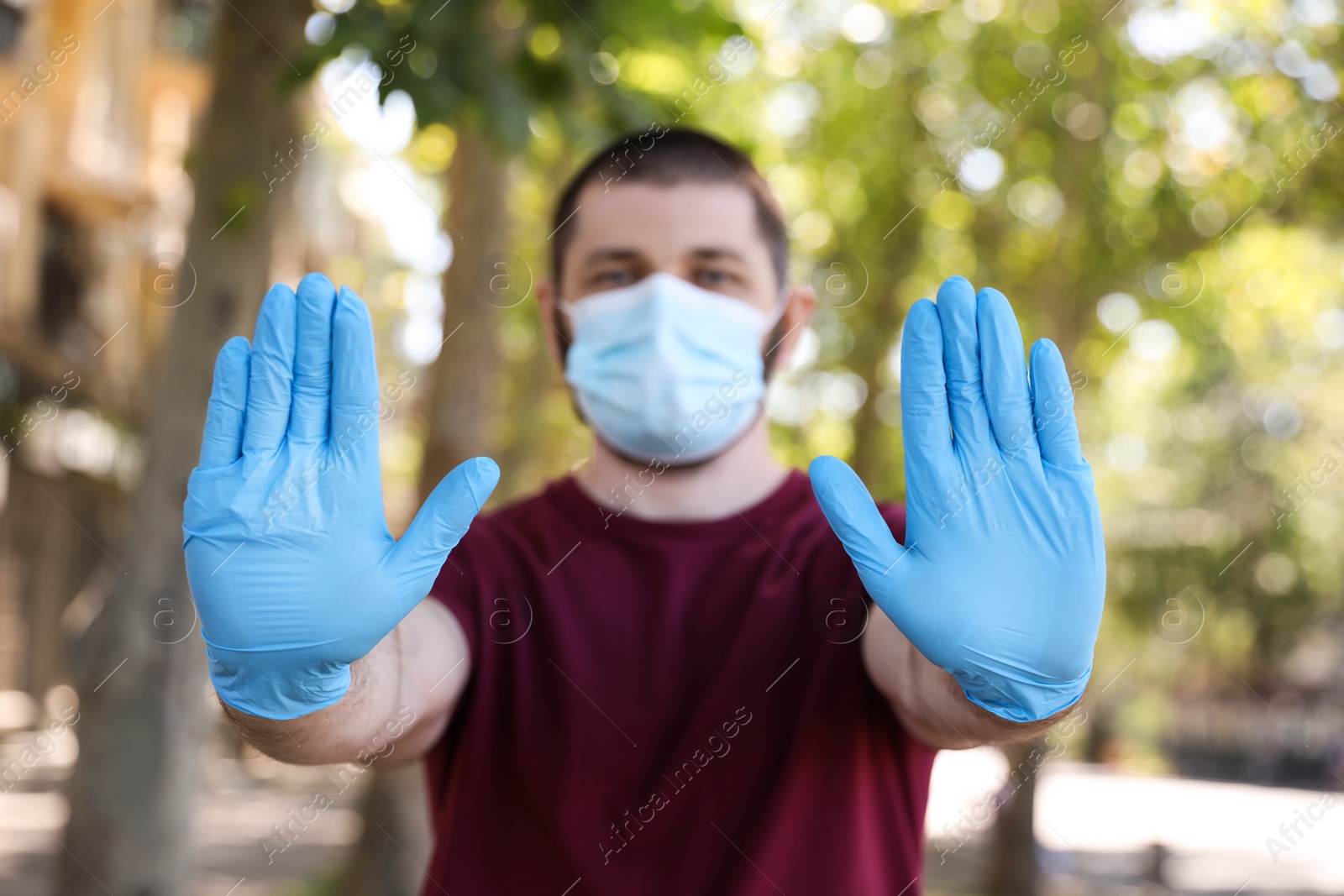 Photo of Man in protective face mask showing stop gesture outdoors, focus on hands. Prevent spreading of coronavirus