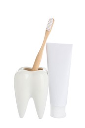 Photo of Tooth shaped holder with brush near tube of toothpaste on white background
