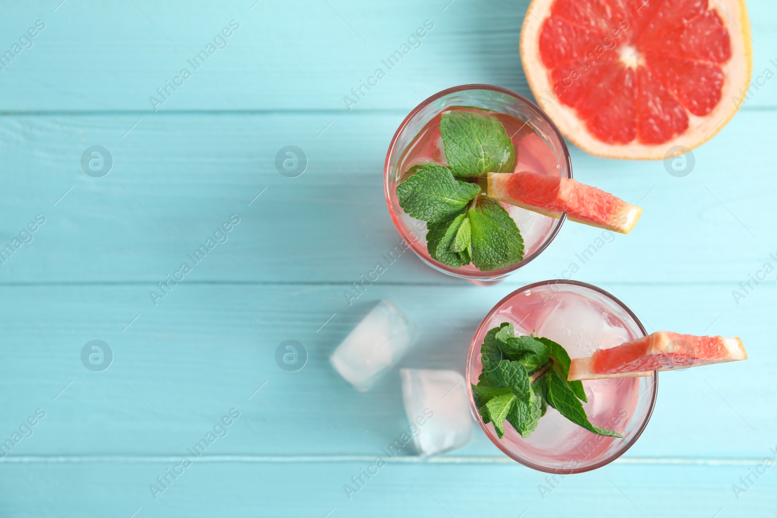 Photo of Glasses of grapefruit cocktails with ice on wooden table, flat lay. Space for text