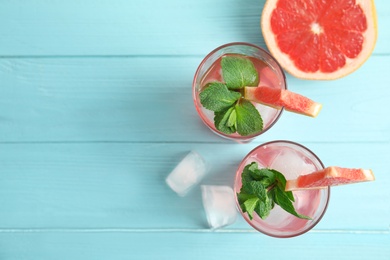 Photo of Glasses of grapefruit cocktails with ice on wooden table, flat lay. Space for text