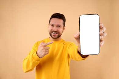 Photo of Handsome man showing smartphone in hand and pointing at it on light brown background, selective focus. Mockup for design