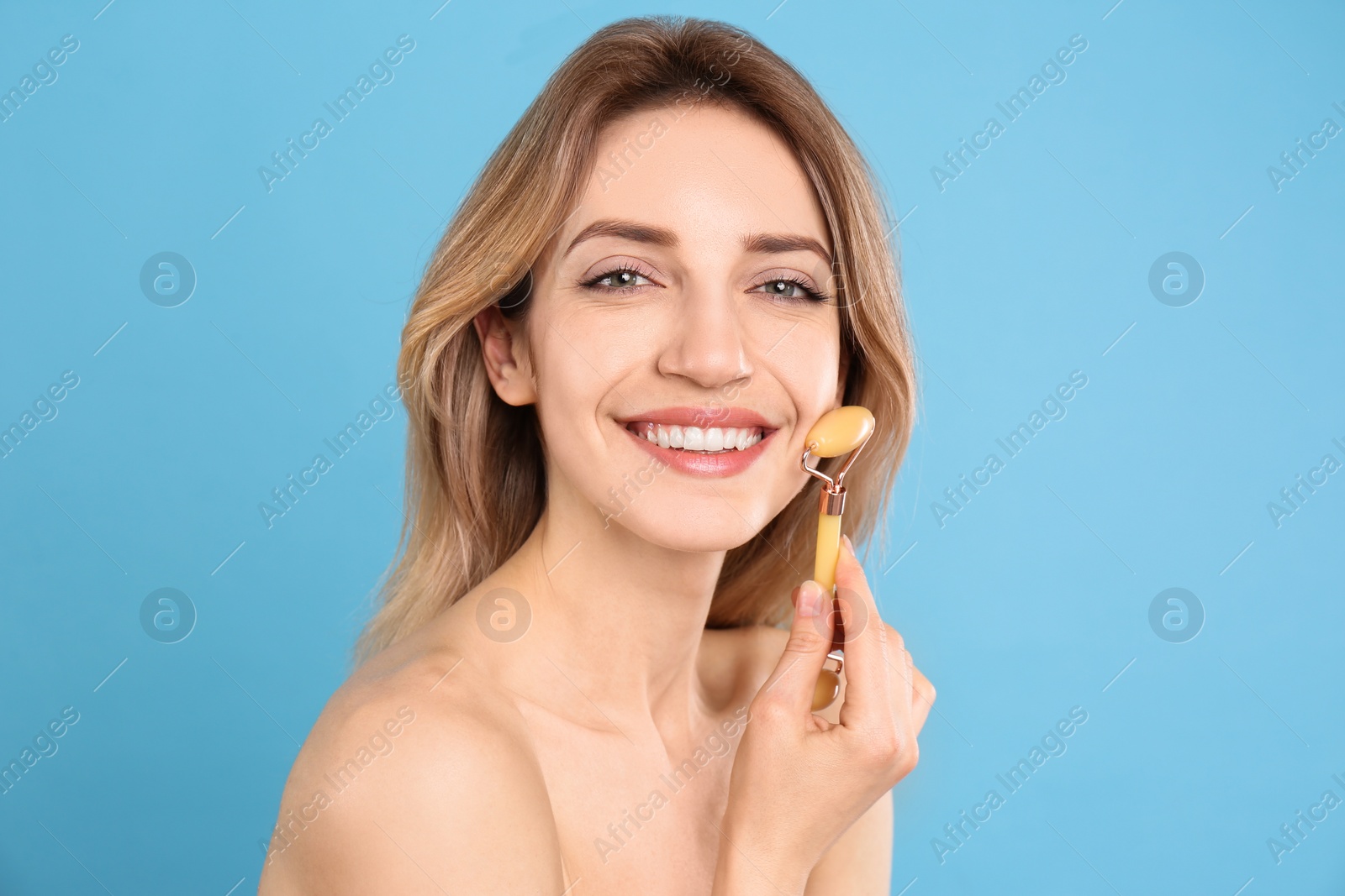 Photo of Young woman using natural jade face roller on light blue background