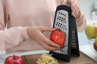 Photo of Woman grating fresh red apple at kitchen table, closeup