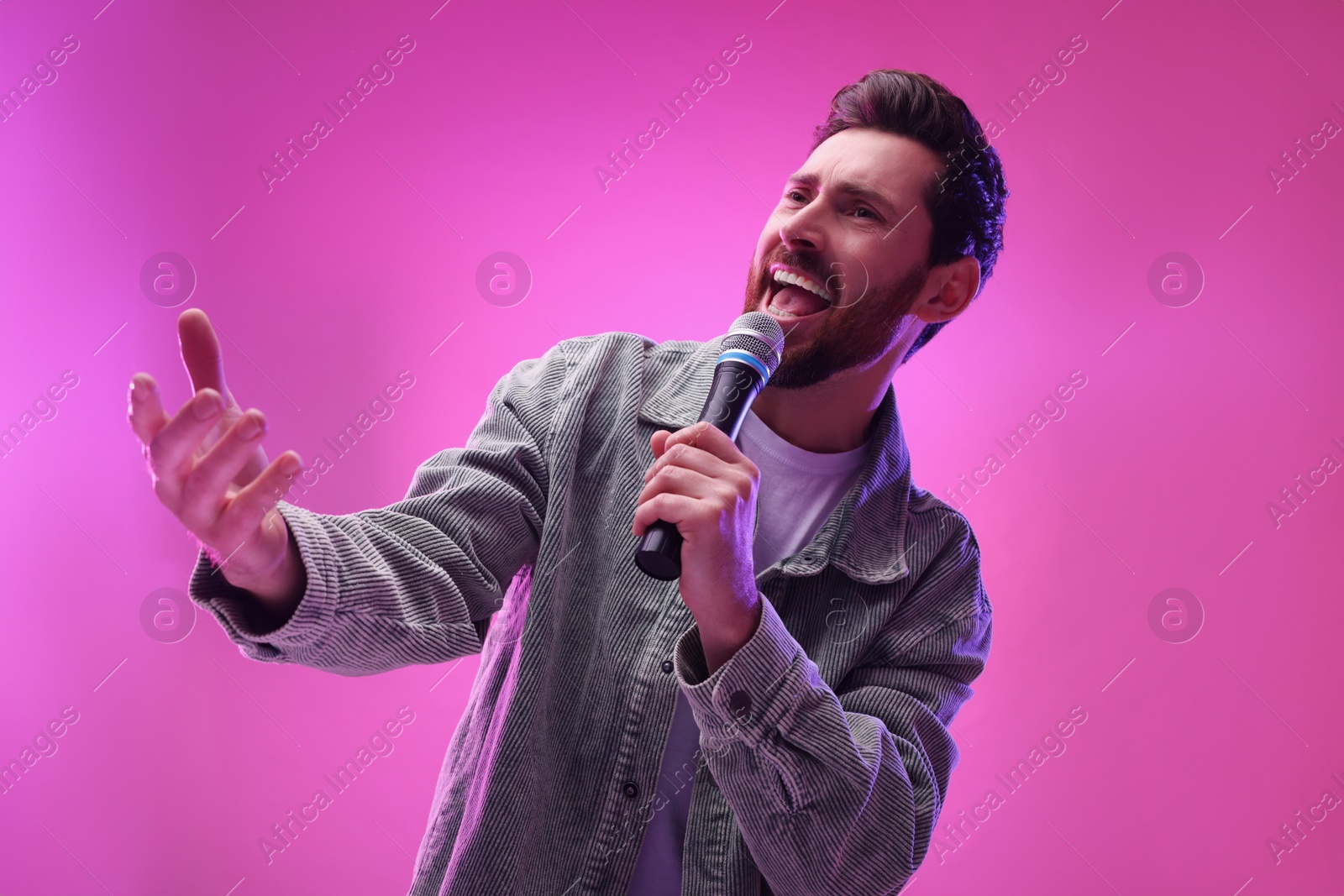 Photo of Handsome man with microphone singing on pink background