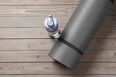 Photo of Yoga mat and bottle of water on grey wooden floor, flat lay. Space for text