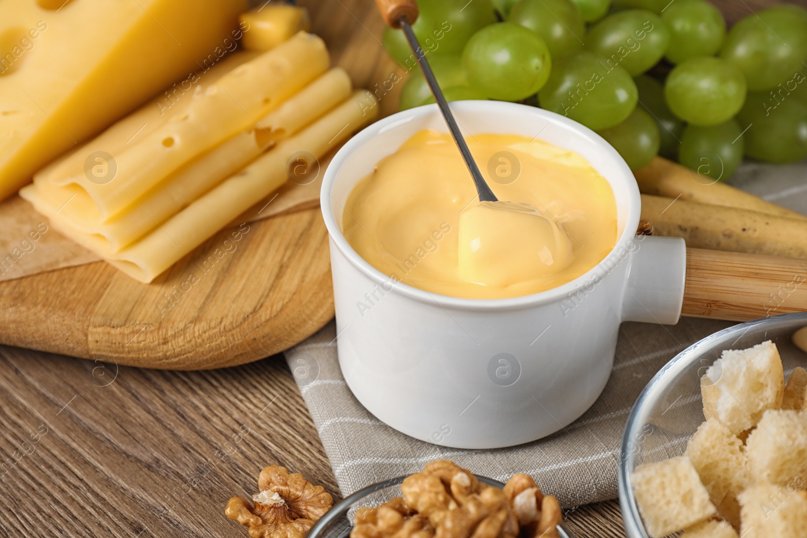 Photo of Pot of tasty cheese fondue and fork with bread on wooden table