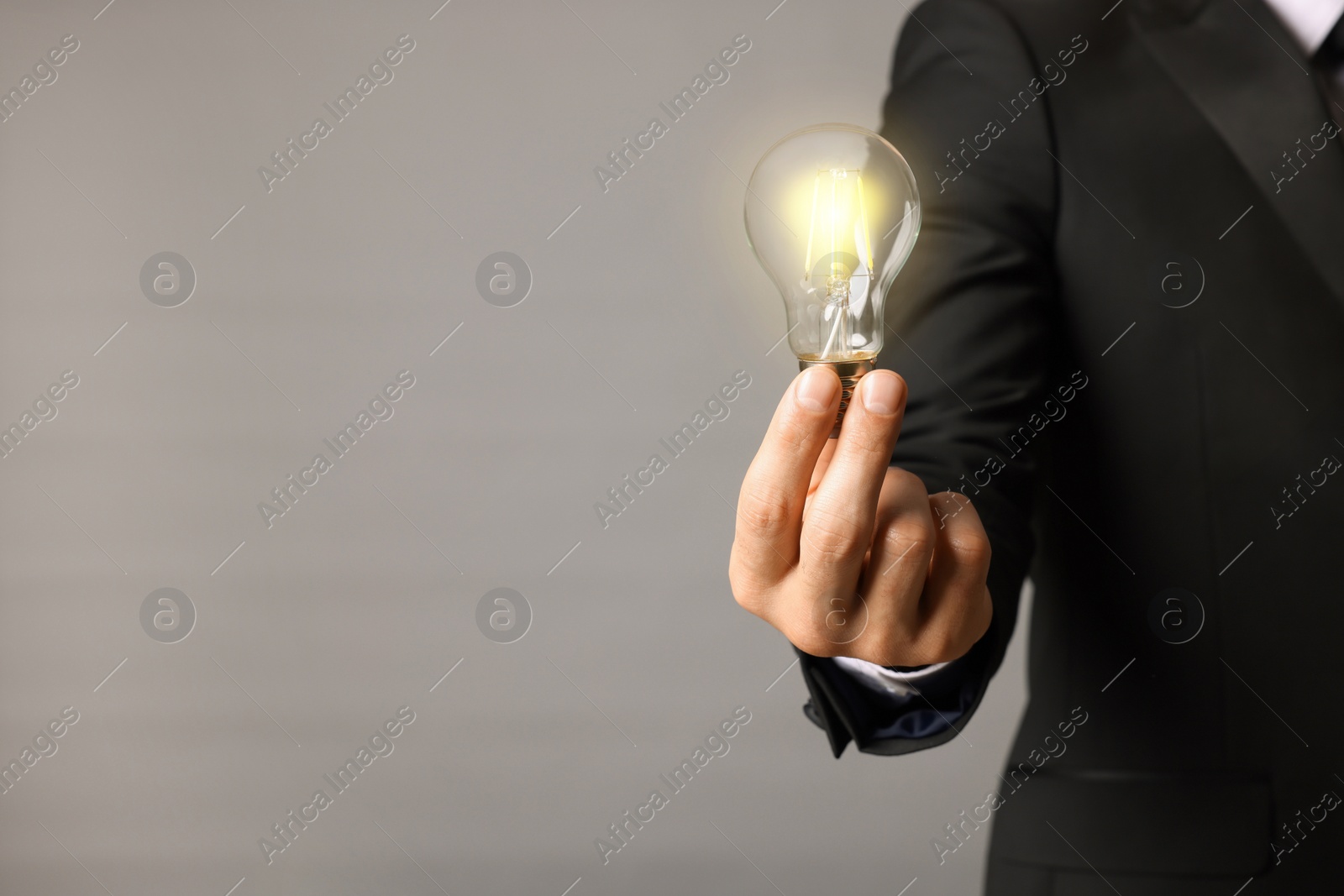 Photo of Glow up your ideas. Closeup view of businessman holding light bulb on grey background, space for text