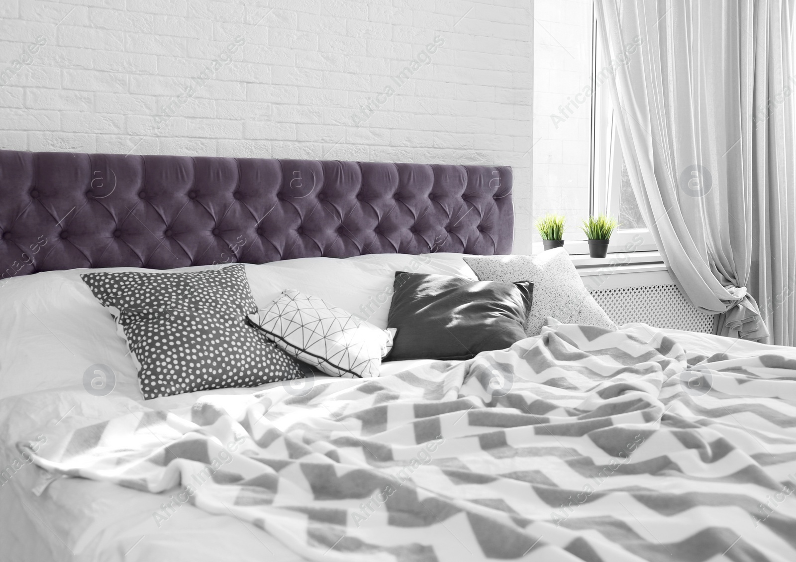 Photo of Bed with pillows and plaid near brick wall. Interior design