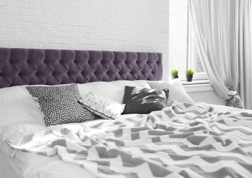 Photo of Bed with pillows and plaid near brick wall. Interior design